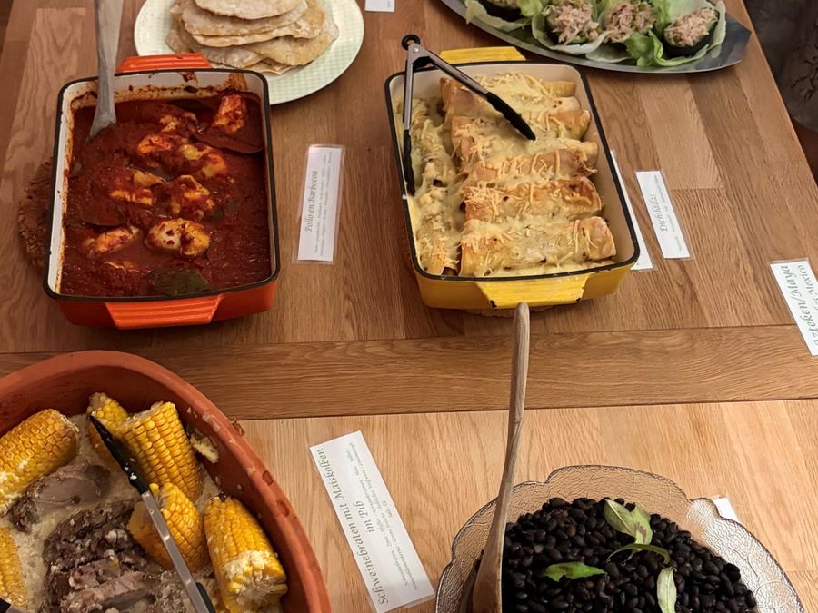 Buffet mit Tortillas, Maiskolben, schwarzen Bohnen und einem Schmortopf, jede Schale mit einem beschrifteten Kärtchen