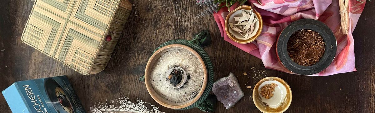 R&auml;ucherschale mit Sand und Kohle, daneben Harze, Salbei, ein M&ouml;rser mit R&auml;ucherwerk und ein Amethyst auf einem dunklen Holztisch